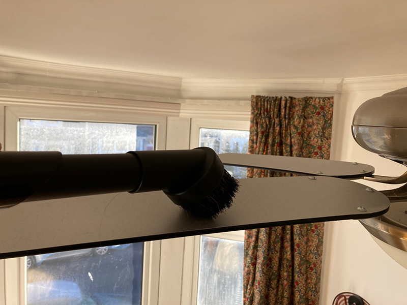 The soft dusting brush attachment for the James vacuum being used to clean a ceiling fan.